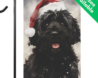 May include: A garden flag featuring a watercolor-style portrait of a black dog wearing a red and white Santa hat. The dog has brown eyes and its tongue is visible. The flag is displayed on a black metal stand.