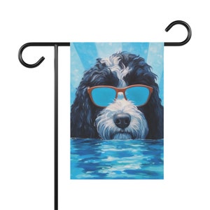 May include: A black and white dog with blue sunglasses is swimming in a pool. The dog is looking at the camera. The background is a blue sky with sun rays.