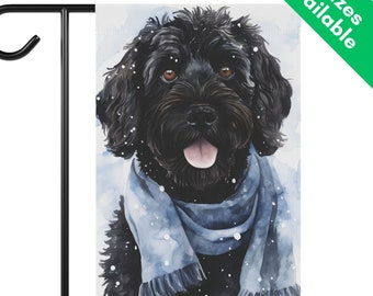 May include: A black dog with a blue scarf is standing in the snow. The dog has a white tongue sticking out and is looking at the camera. The background is a watercolor painting of snow.