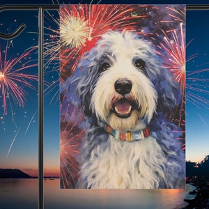 May include: A white and blue Old English Sheepdog with a red, white, and blue collar is in front of a background of fireworks. The dog is smiling and has a happy expression on its face.