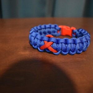 May include: A blue paracord bracelet with a red ribbon woven into the design.