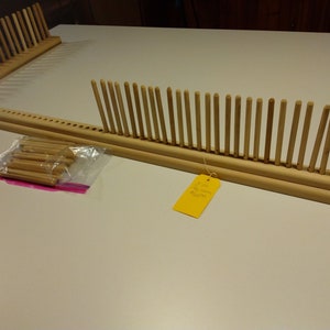 Puede incluir: Un telar de madera con una fila de clavijas de madera, una bolsa de clavijas adicionales y una etiqueta amarilla que dice "12 pulg.  Telar pequeño $ 20.00"