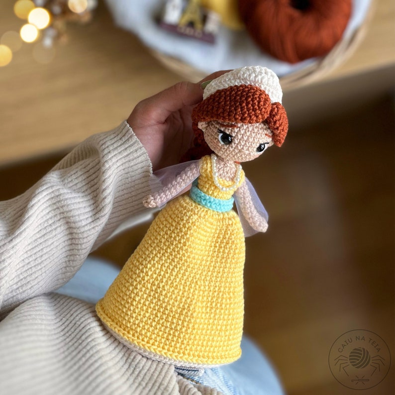 May include: A crocheted doll with a yellow dress, blue sash, and white hat. The doll has brown hair and a sweet expression.