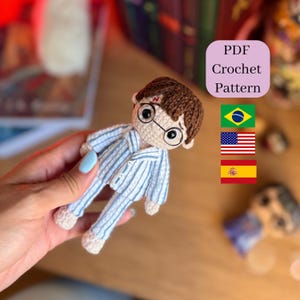 Pode incluir: Boneca de crochê de um personagem com cabelo castanho, óculos redondos e uma cicatriz de raio na testa. A boneca está vestindo um pijama listrado azul e branco. A imagem inclui o texto "PDF Crochet Pattern" e bandeiras do Brasil, EUA e Espanha.