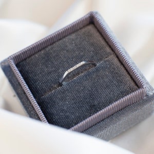 May include: A silver ring with small diamonds set in a band. The ring is displayed in a gray velvet ring box.