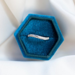 May include: A silver ring with small diamonds set in a curved band, displayed in a teal blue velvet ring box.