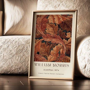 Op de afbeelding: Een ingelijste print van een vintage botanische illustratie met een herhalend patroon van gestileerde bladeren in tinten oranje, rood en bruin. De print is getiteld "William Morris, Acanthus, 1874, Classic Textile Pattern Collection".