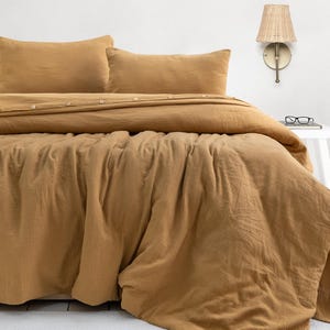 May include: A mustard yellow duvet cover set featuring a textured, crinkled fabric finish. The bedding includes two matching rectangular pillow shams and a large duvet cover with a button-down closure detail along the top edge.