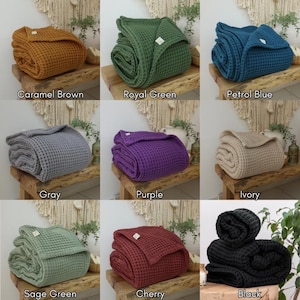 May include: Nine waffle weave blankets in various colors, including caramel brown, royal green, petrol blue, gray, purple, ivory, sage green, cherry, and black. The blankets are folded and displayed on wooden benches.