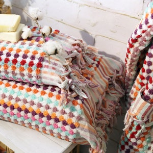 May include: Two colourful Turkish towels with fringe, stacked on a white surface. The towels have a pattern of small, colourful circles and stripes. The towels are made of cotton and are soft and absorbent.