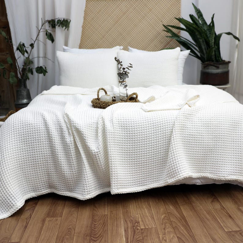 May include: White waffle weave throw blanket on a bed with white pillows. The blanket is folded back to reveal the white sheets underneath.