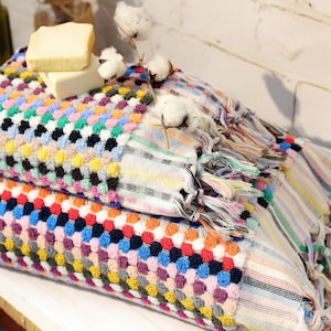 May include: Two colourful Turkish towels with fringe, one stacked on top of the other. The top towel has a pattern of small, colourful circles and stripes. The bottom towel has a similar pattern with larger circles. The towels are decorated with cotton bolls.