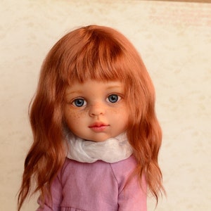 May include: A doll with long, wavy, red hair wearing a pink dress and brown boots. The doll is sitting on a wooden box.