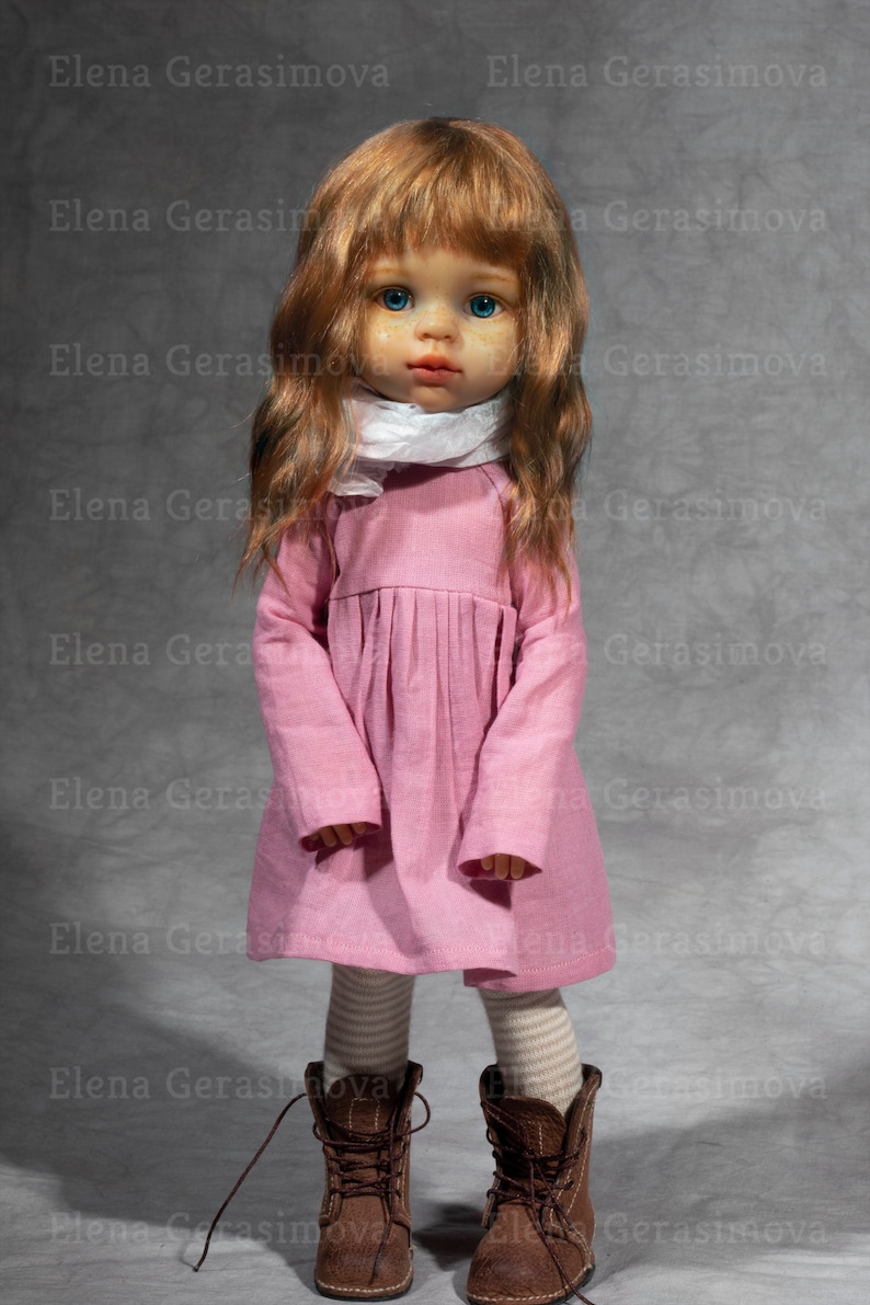 May include: A doll with long, wavy, auburn hair, blue eyes, and freckles wearing a pink dress, white scarf, and brown boots.