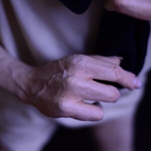 Puede incluir: Primer plano de una mano, mostrando las venas y las arrugas de la piel. La mano sostiene un trozo de tela oscura.