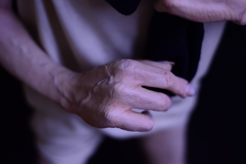 Puede incluir: Primer plano de una mano, mostrando las venas y las arrugas de la piel. La mano sostiene un trozo de tela oscura.
