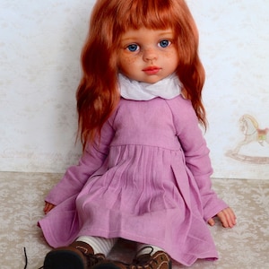 May include: A red-haired doll wearing a pink dress and brown shoes. The doll has blue eyes and freckles.