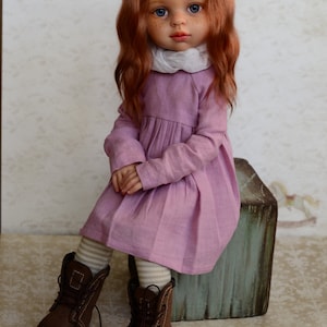 May include: A doll with long, wavy, red hair wearing a pink dress and brown boots. The doll is sitting on a wooden box.
