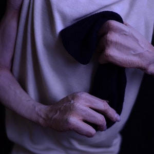 May include: A person wearing a white vest top is holding a black sock in their hands.