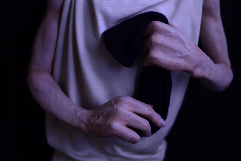May include: A person wearing a white vest top is holding a black sock in their hands.