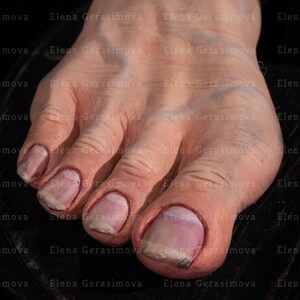 Puede incluir: Primer plano de un pie descalzo con cinco dedos. Los dedos est&aacute;n pintados con un esmalte rosa claro y tienen una textura ligeramente rugosa. El pie est&aacute; apoyado sobre una superficie de madera oscura.