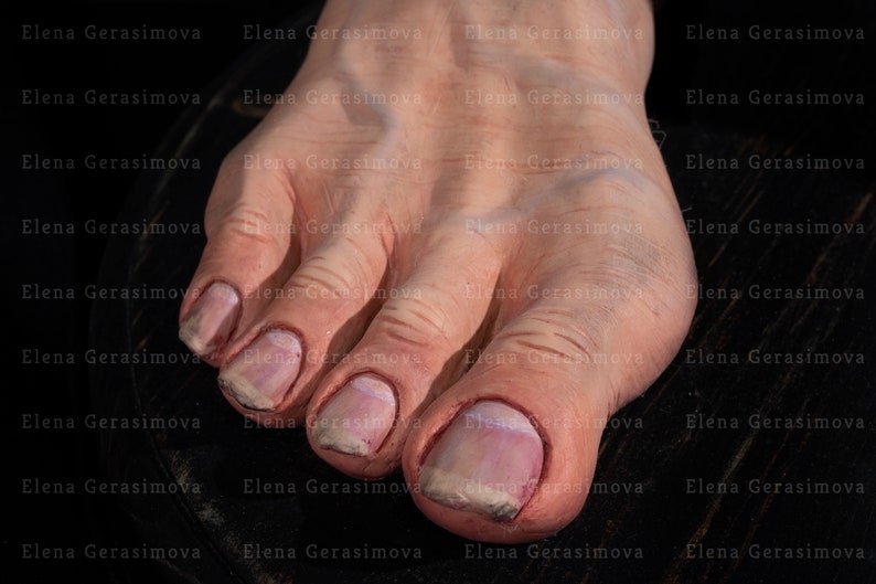 Puede incluir: Primer plano de un pie descalzo con cinco dedos. Los dedos est&aacute;n pintados con un esmalte rosa claro y tienen una textura ligeramente rugosa. El pie est&aacute; apoyado sobre una superficie de madera oscura.