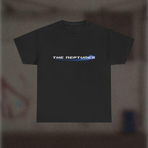 May include: Black t-shirt with the text "THE NEPTUNES" in white and blue. The text is centered on the chest of the shirt. The shirt has short sleeves and a crew neck.