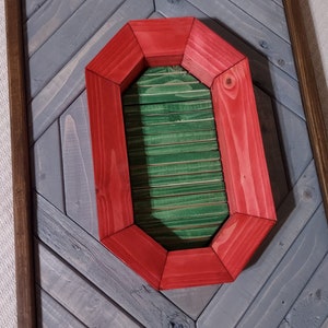 May include: A red wooden frame in the shape of the letter "O" with a green wooden interior. The frame is mounted on a gray wooden background.