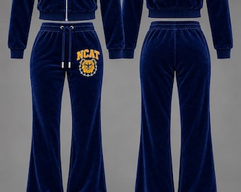 May include: A navy blue velour tracksuit featuring a zip-up hoodie and matching pants. The hoodie has a hood, silver zipper, and NCAT bulldog logo on the chest. The back displays NCAT Aggie Pride text. Pants include a drawstring waist and logo.
