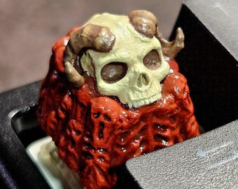 Puede incluir: Una tecla personalizada para teclado mecánico con un diseño esculpido y pintado a mano de un cráneo beige con cuernos curvos sobre una base roja profunda y texturizada con detalles orgánicos intrincados similares a huesos.