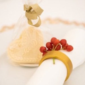Könnte beinhalten: Eine weiße Serviette mit einem goldenen Serviettenring und roten Beeren. Eine kleine, transparente Tüte mit einem goldenen Band enthält einen weißen Keks.