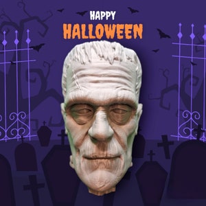 May include: A white, sculpted face of a monster with a stitched scar across the forehead. The face is against a purple background with black silhouettes of trees and gates. The text "Happy Halloween" is at the top of the image.