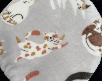May include: A round, gray cat bed with a plush texture. The bed is decorated with playful illustrations of cats in various poses, featuring white, brown, and orange markings. The overall design is soft and inviting.