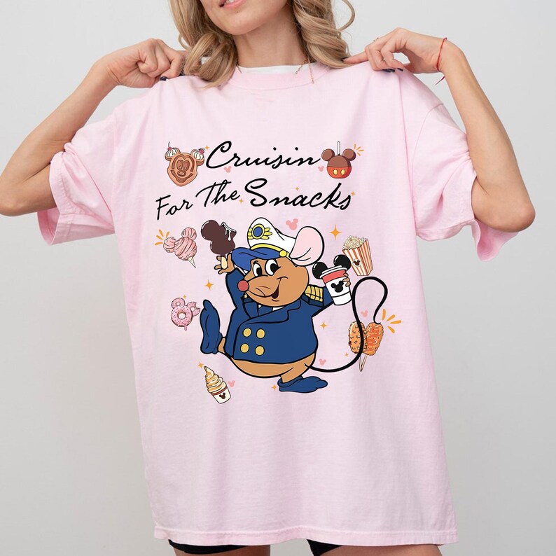 May include: A light pink t-shirt with the phrase "Cruisin' For the Snacks" and a cartoon mouse in a navy blue uniform. The mouse is holding a coffee cup and a chocolate-covered ice cream cone, surrounded by snacks.