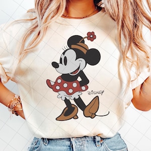 May include: Cream-colored sweatshirt featuring a graphic of Minnie Mouse in a red polka-dot skirt, brown shoes, and a flower on her head. The Disney logo is printed below the character.