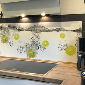 Könnte beinhalten: Eine Küchenrückwand mit einem Design aus Wasser, Limettenscheiben und Eiswürfeln. Das Bild hat einen weißen Hintergrund mit schwarzen und grauen Akzenten. Die Rückwand ist über einem schwarzen Kochfeld installiert.