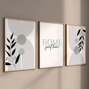 Peut inclure: Ensemble de trois impressions d'art encadrées. Les impressions présentent des motifs abstraits avec des lignes noires, des cercles vert sauge et des accents de feuilles noires. L'impression centrale porte l'inscription "HOME sweet home" en vert sauge et noir.