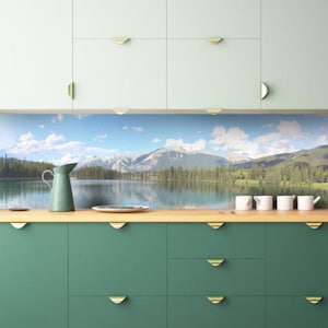 Peut inclure: Une crédence de cuisine avec un paysage de montagne et de lac forestier. La crédence est installée au-dessus de placards verts avec des poignées dorées.