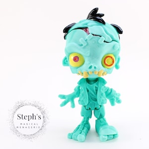 May include: A teal green zombie toy with black hair, yellow eyes, and a cracked skull. The toy has a skeleton-like body and is posed with its arms outstretched.