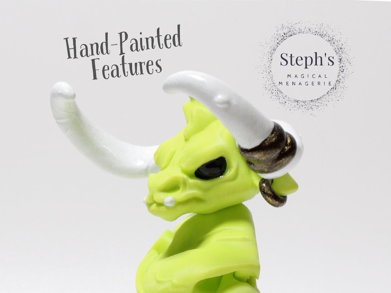 May include: A hand-painted, lime green figurine of a horned creature with white horns and black eyes. The figurine has a gold earring and a small white tooth. The text "Hand-Painted Features" is visible. The Steph's Magical Menagerie logo is also visible.