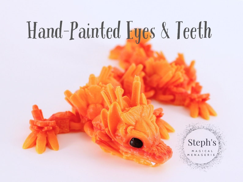 Pu&ograve; includere: Due figurine di drago arancioni e gialle dipinte a mano con squame dettagliate e occhi e denti dipinti a mano. Le figurine sono su uno sfondo bianco. Steph's Magical Menagerie.