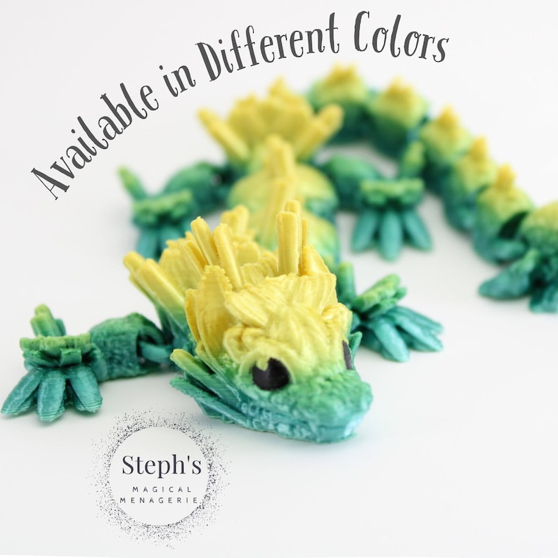 Pu&ograve; includere: Tre piccole figurine di drago stampate in 3D in tonalit&agrave; di verde e giallo. I draghi sono in una posizione giocosa, arrotolati. Il testo "Available in Different Colors" &egrave; scritto nell'angolo in alto a sinistra dell'immagine.