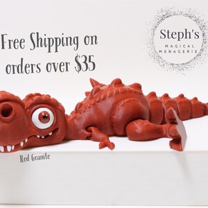 May include: Red granite dinosaur figurine with a large eye, lying on a white surface. The text "Free Shipping on orders over &pound;35" is visible above the dinosaur. The text "Steph's Magical Menagerie" is visible in the upper right corner of the image.