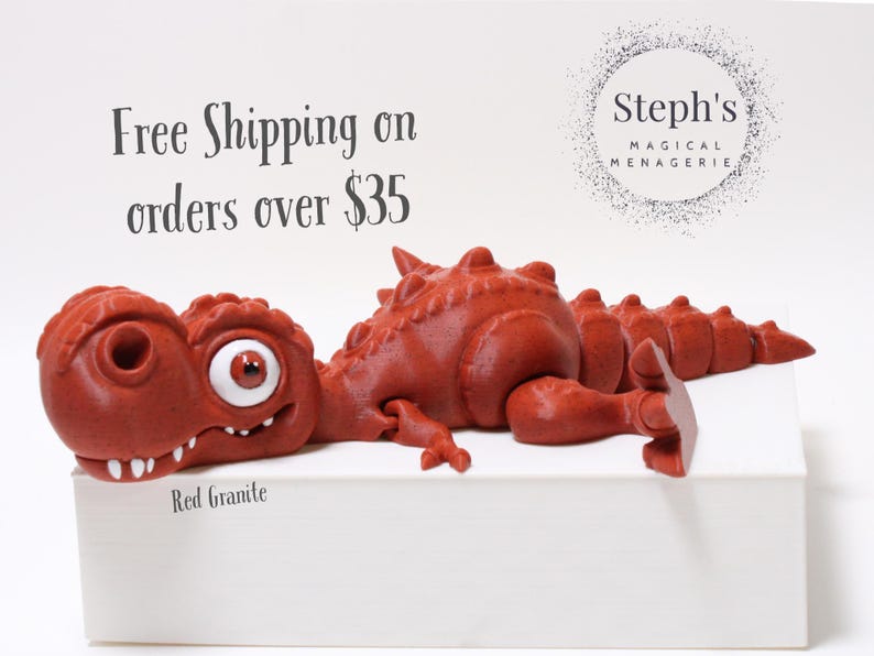 May include: Red granite dinosaur figurine with a large eye, lying on a white surface. The text "Free Shipping on orders over &pound;35" is visible above the dinosaur. The text "Steph's Magical Menagerie" is visible in the upper right corner of the image.