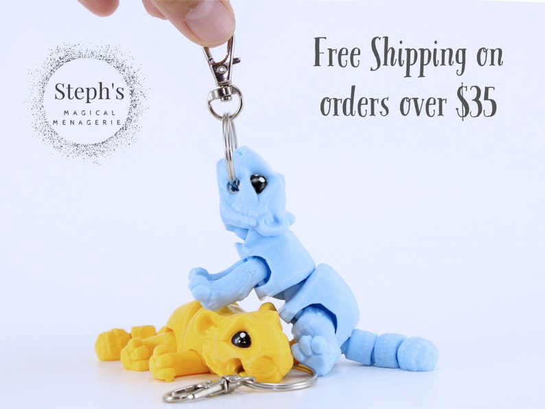 May include: Two small, articulated, 3D printed animal figures. The blue figure is on top of the yellow figure. Both figures are attached to a silver key chain.