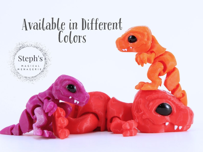 May include: Three articulated dinosaur toys in the image. One is red, one is purple, and the other is orange. The toys have black eyes and are on a white background. The text "Available in Different Colors" is at the top.