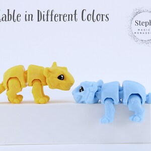 May include: Two small, articulated animal figurines, one yellow and one blue, are posed on a white surface. The yellow figurine is a tiger and the blue figurine is a bear. The text "Steph's Magical Menagerie" is visible in the background.