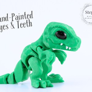 May include: A green articulated dinosaur figurine with hand-painted eyes and teeth. The figurine has a textured surface and is posed on a white background. The text "Hand-Painted Eyes & Teeth" is visible.