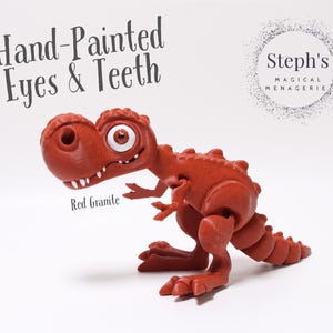 May include: Hand-painted red dinosaur toy with a toothy grin and large eyes. The toy is made of a textured material and is labelled "Red Granite". The image also includes the text "Steph's Magical Menagerie".