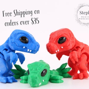May include: Three articulated dinosaur figurines in blue, red, and green are displayed against a white background. The blue and red dinosaurs stand upright, while the green one lies flat. The image includes the text "Steph's Magical Menagerie."